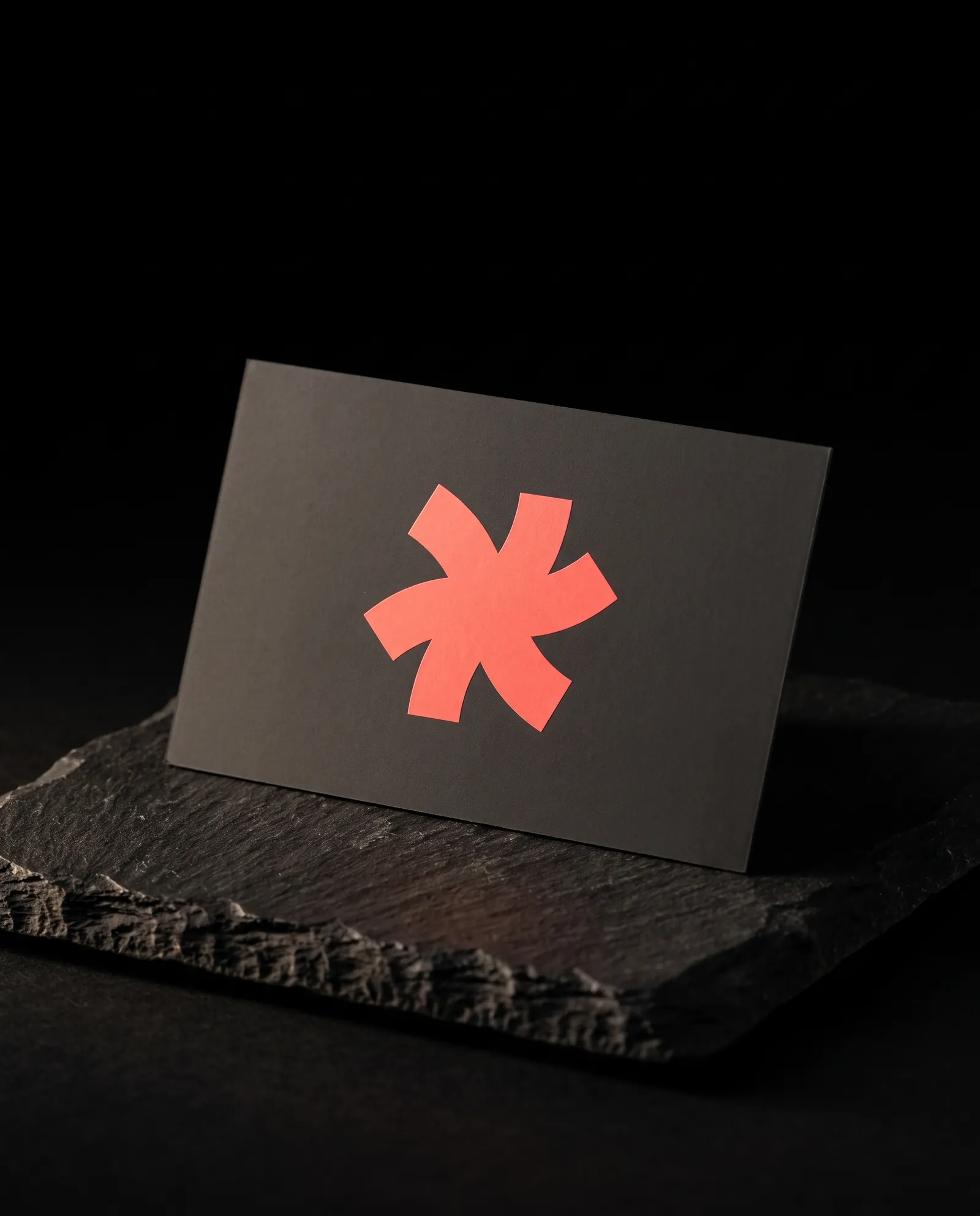 Charcoal 19pt soft-touch business card with a flat coral Print Peppermint mark, velvety with no highlight, on black slate