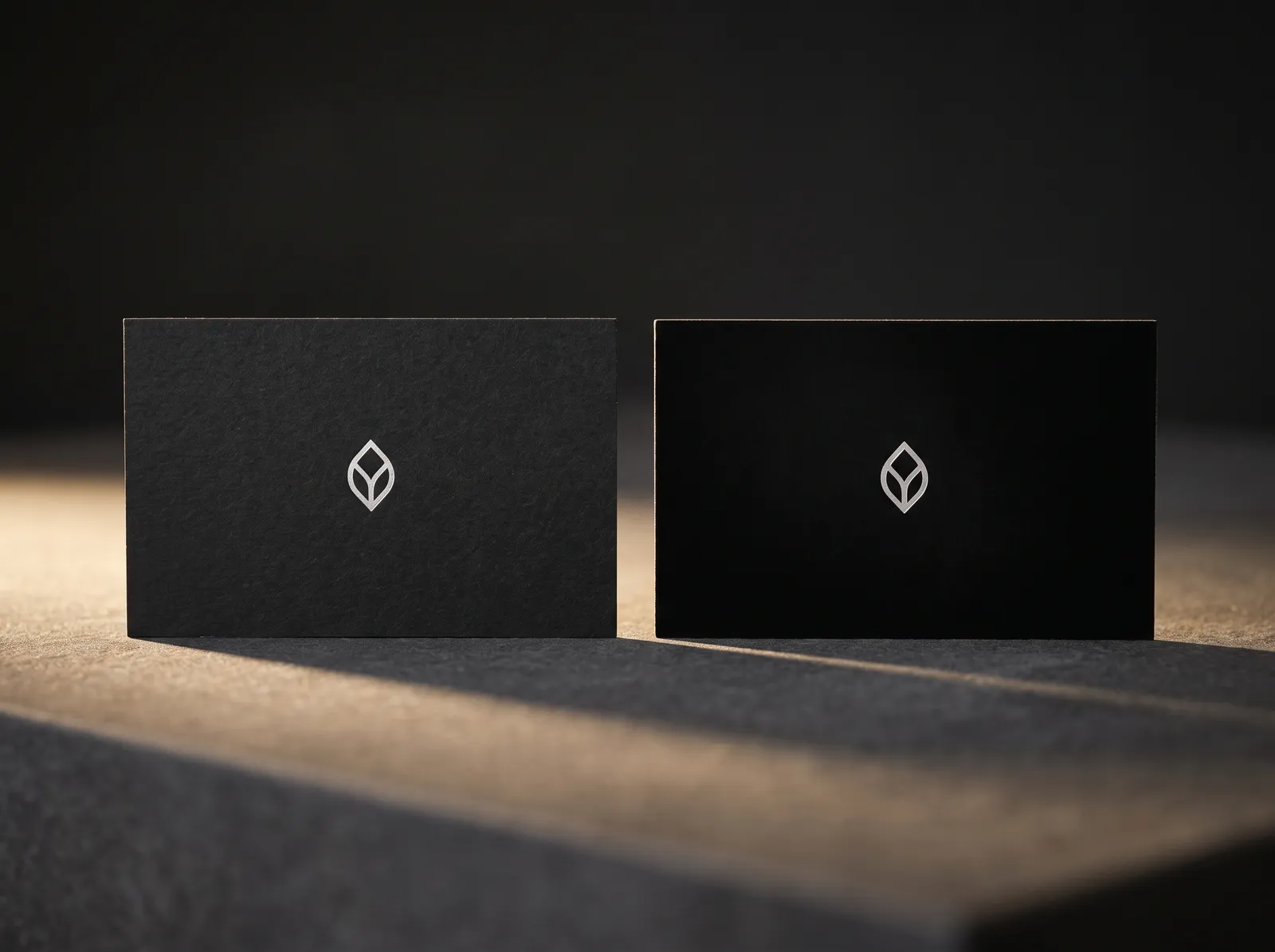 Two matte black business cards side by side, black uncoated with visible fibre and black soft touch with a velvet surface