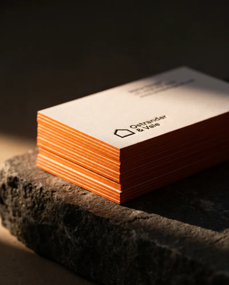 Stack of thick white uncoated business cards with bright orange painted edges on dark stone
