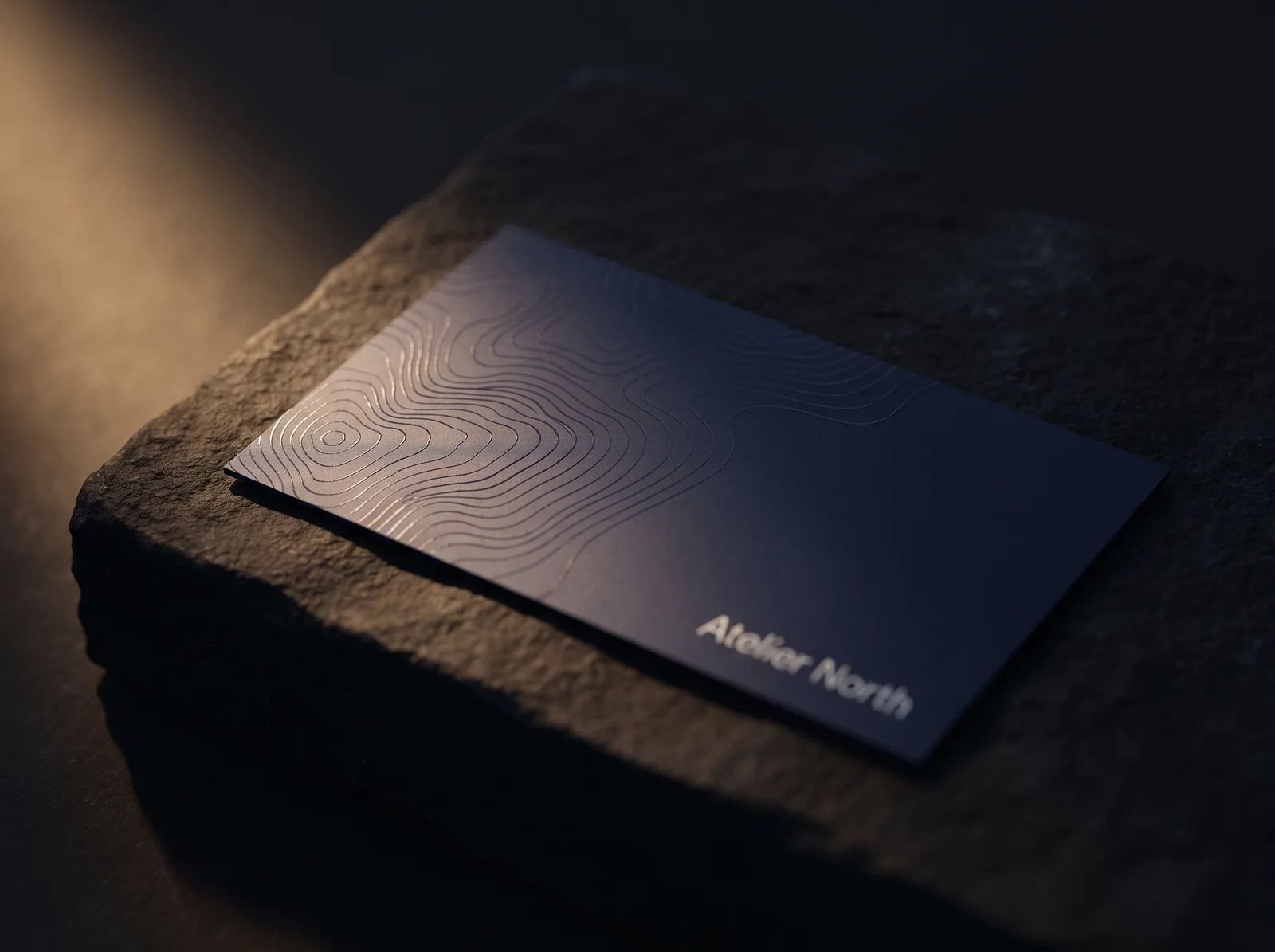 Navy silk business card with flat clear spot UV topographic pattern glinting in warm light