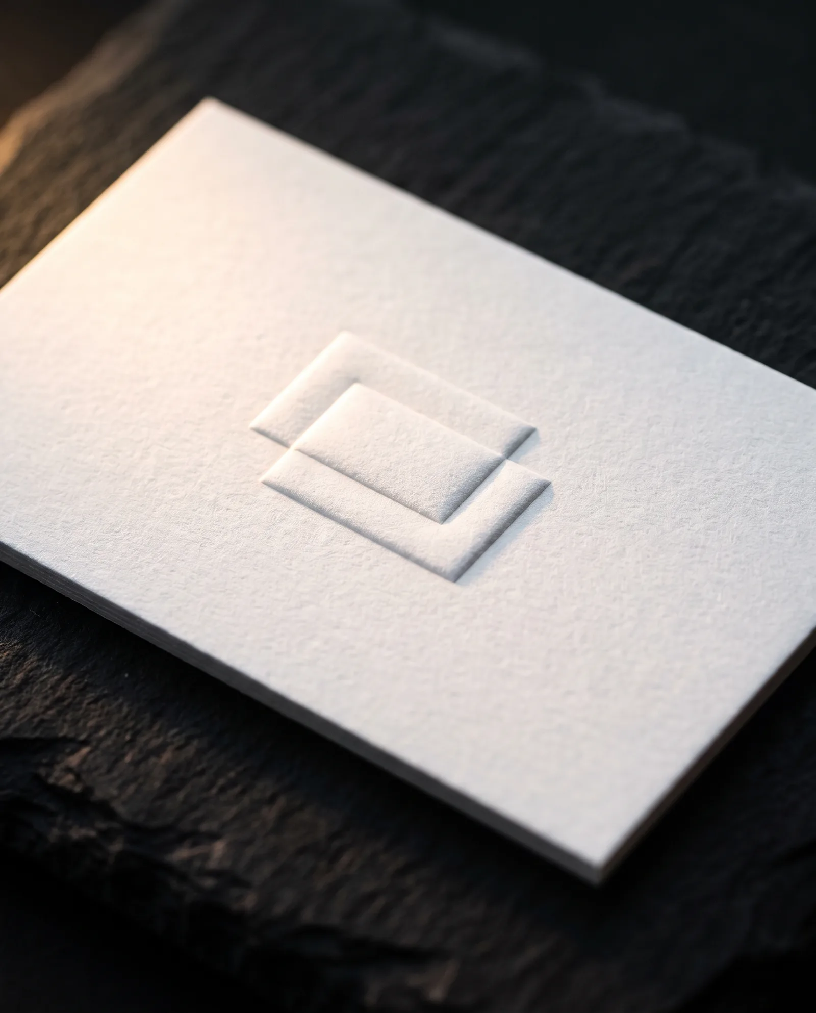 3D embossed business card with a two-level sculpted monogram in raking light