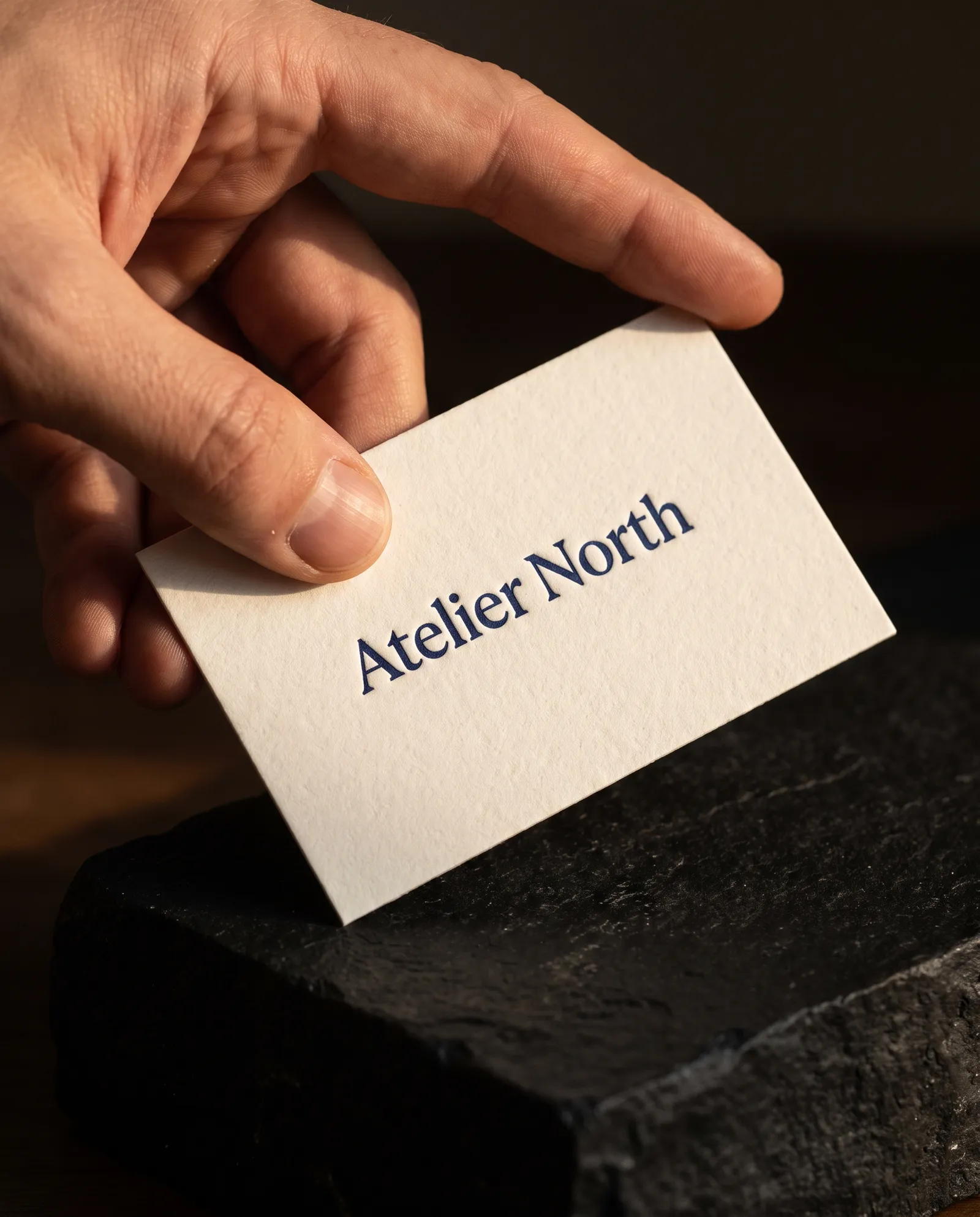 Thumb resting on a letterpress business card, the debossed type catching a raking light on thick cotton