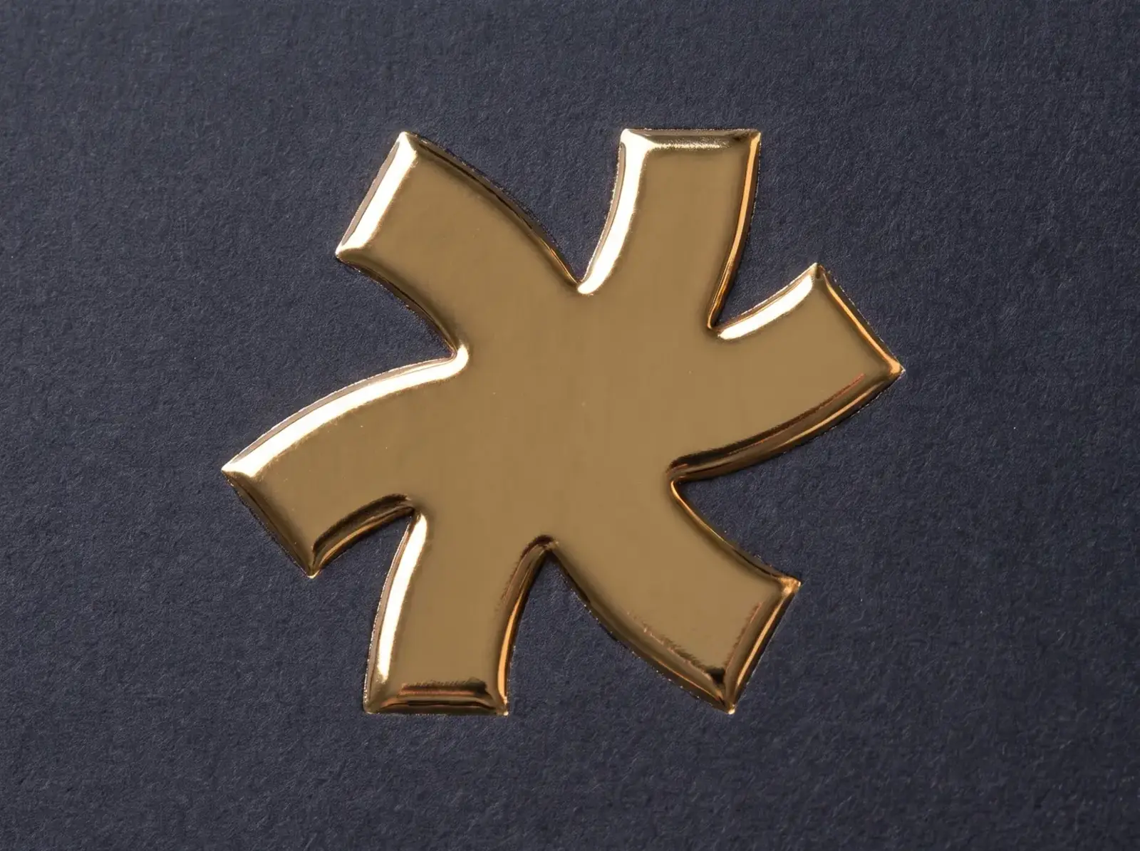 Charcoal soft-touch business card with a raised gold foil pinwheel, the foil standing proud of the velvety surface