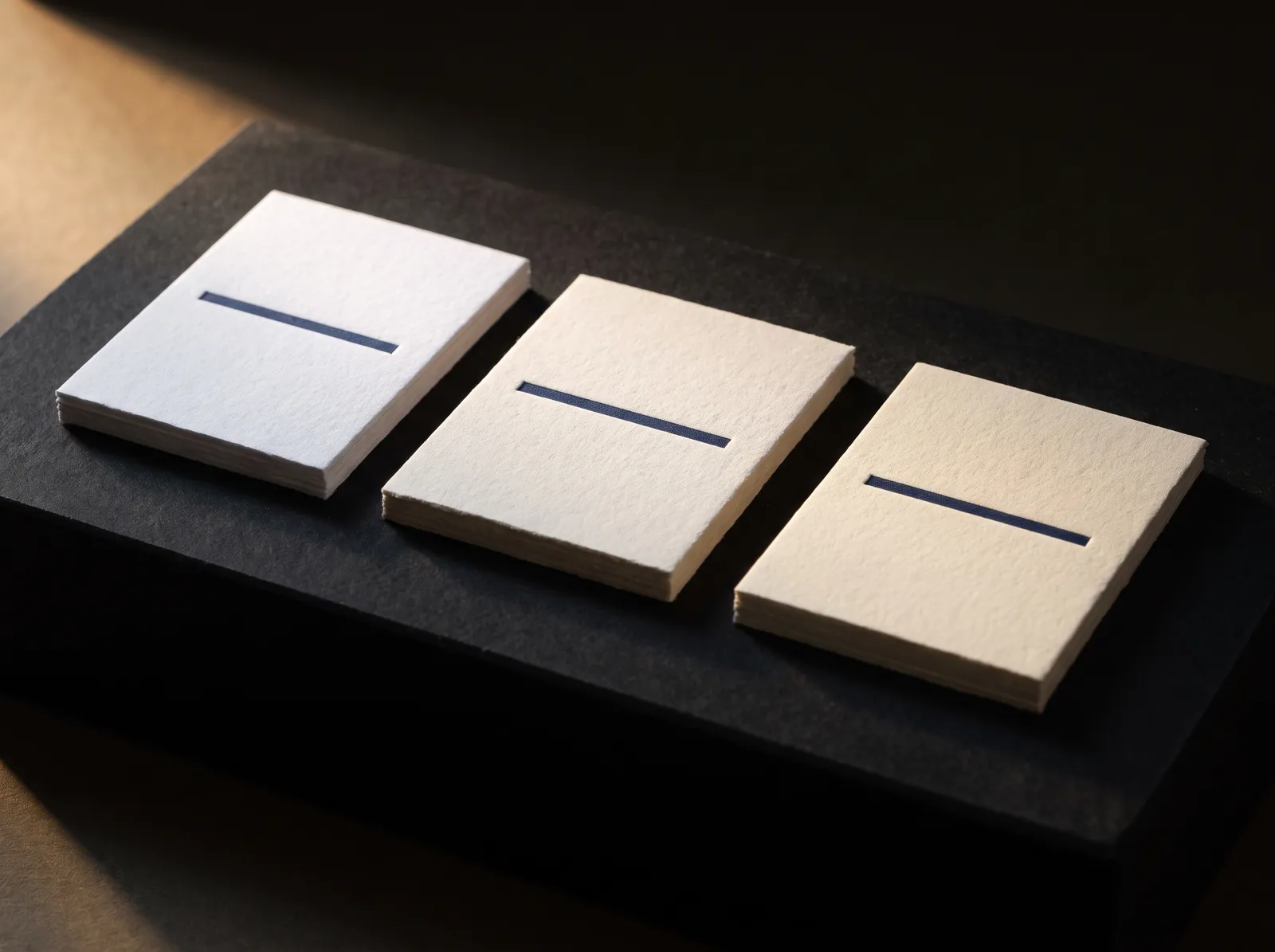 Three cotton letterpress papers, bright white, natural white and ivory, each with the same navy letterpress line showing how the shade tints the ink