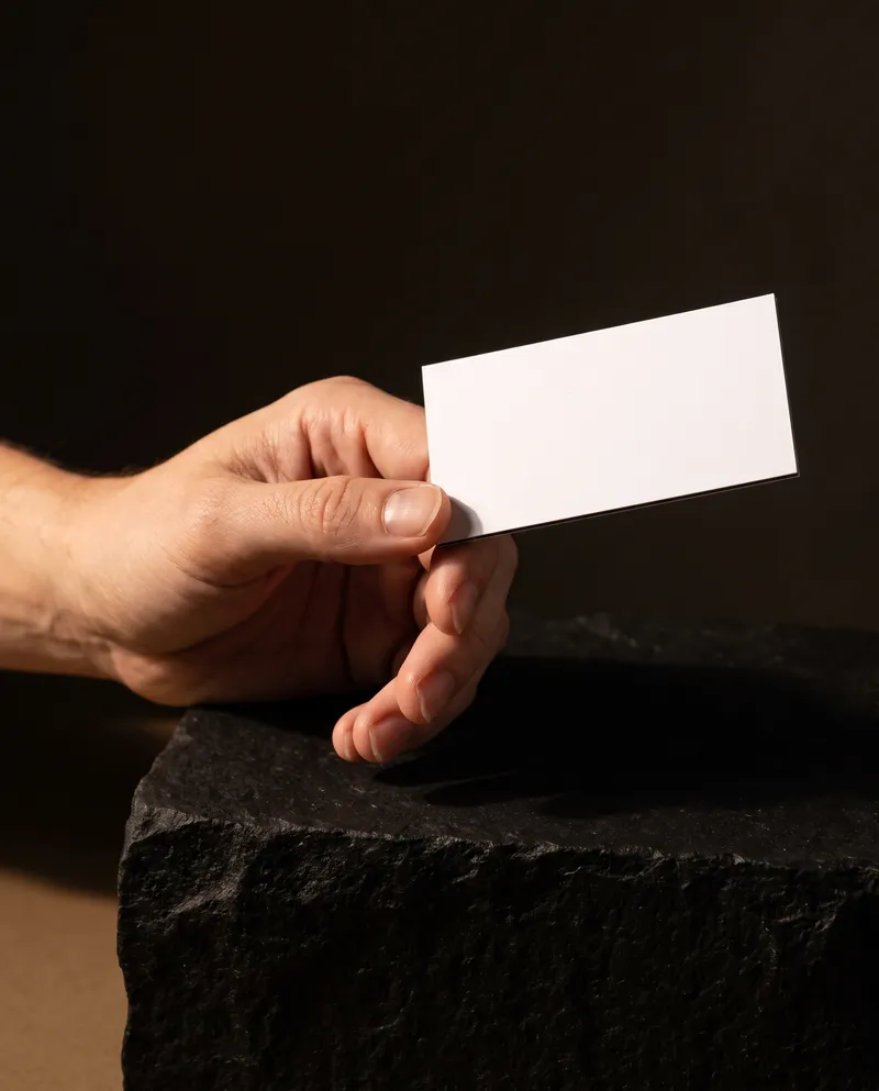 A hand holding a skinny business card between two fingers, the card spanning the fingers with its black core edge visible