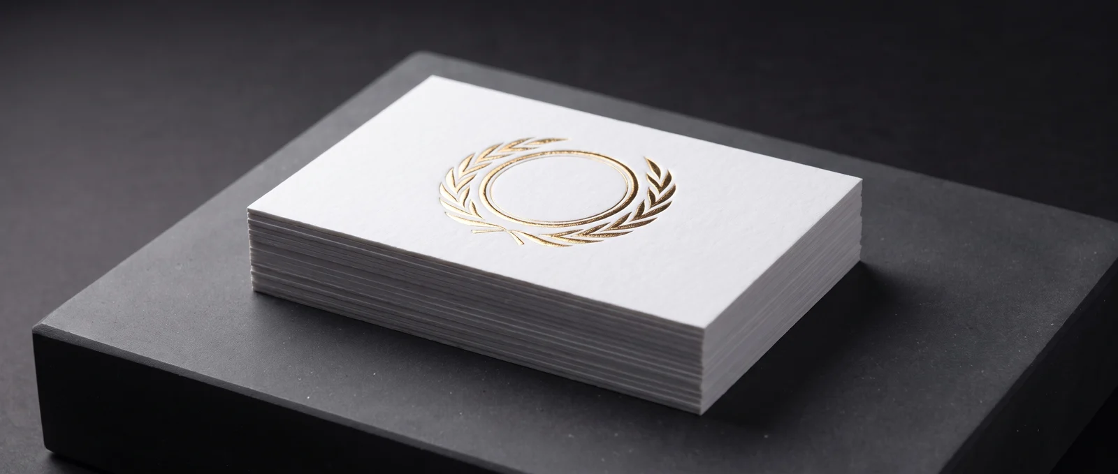 A gold foil mark embossed above white cotton, foil registered to the relief.