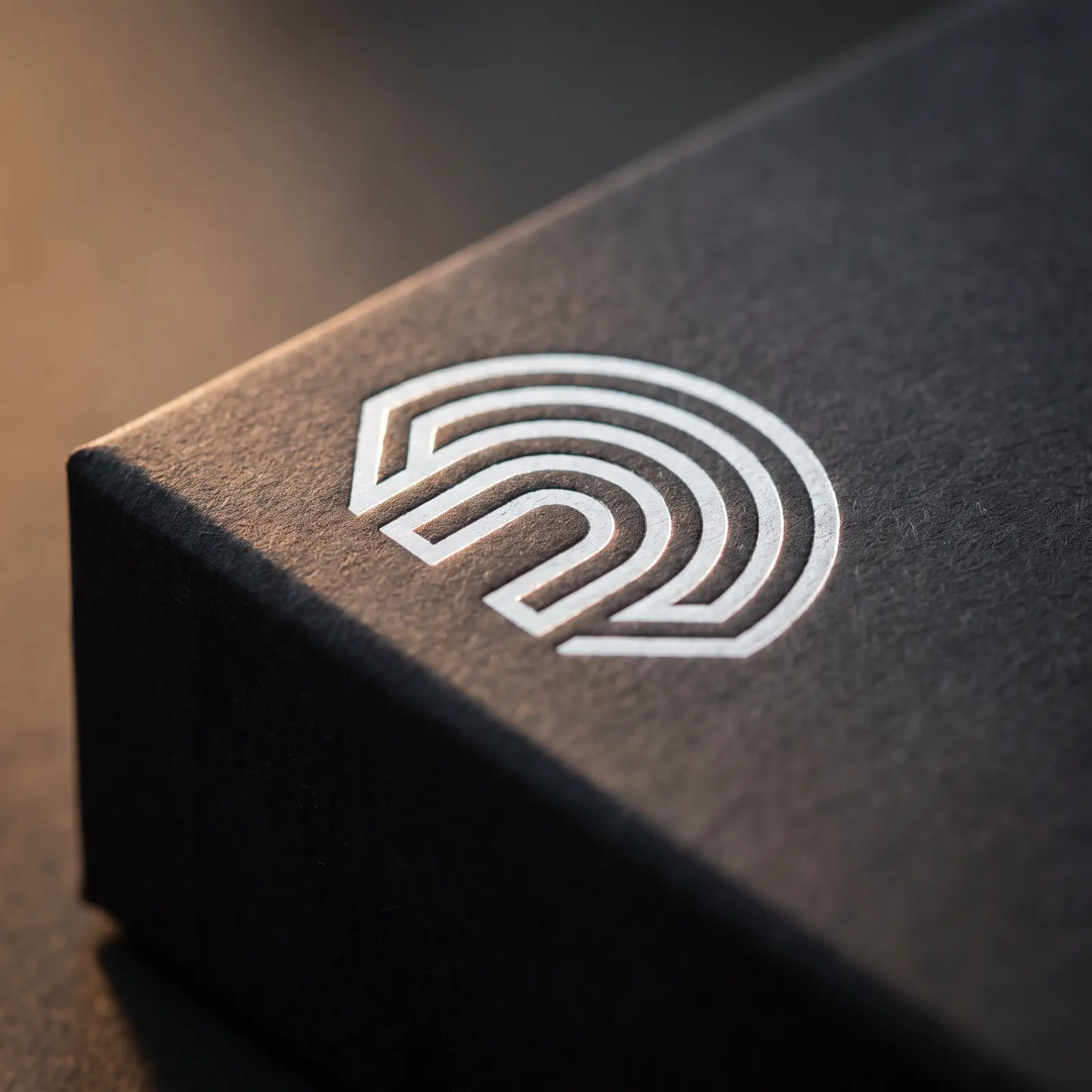 Macro of silver hot foil and shallow deboss on charcoal uncoated box flap, paper fibre