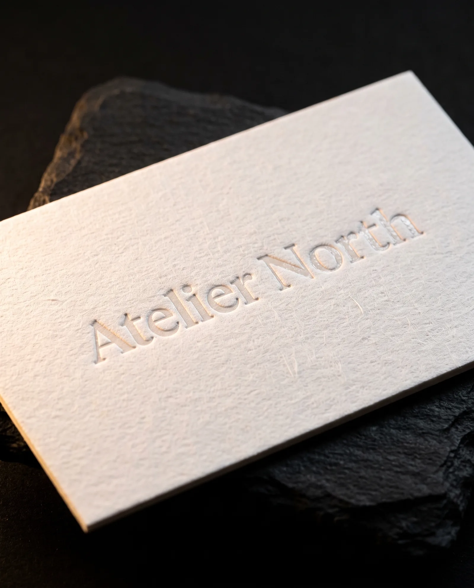 Clear foil wordmark pressed into a thick natural cotton business card, satin shine with a slight bite