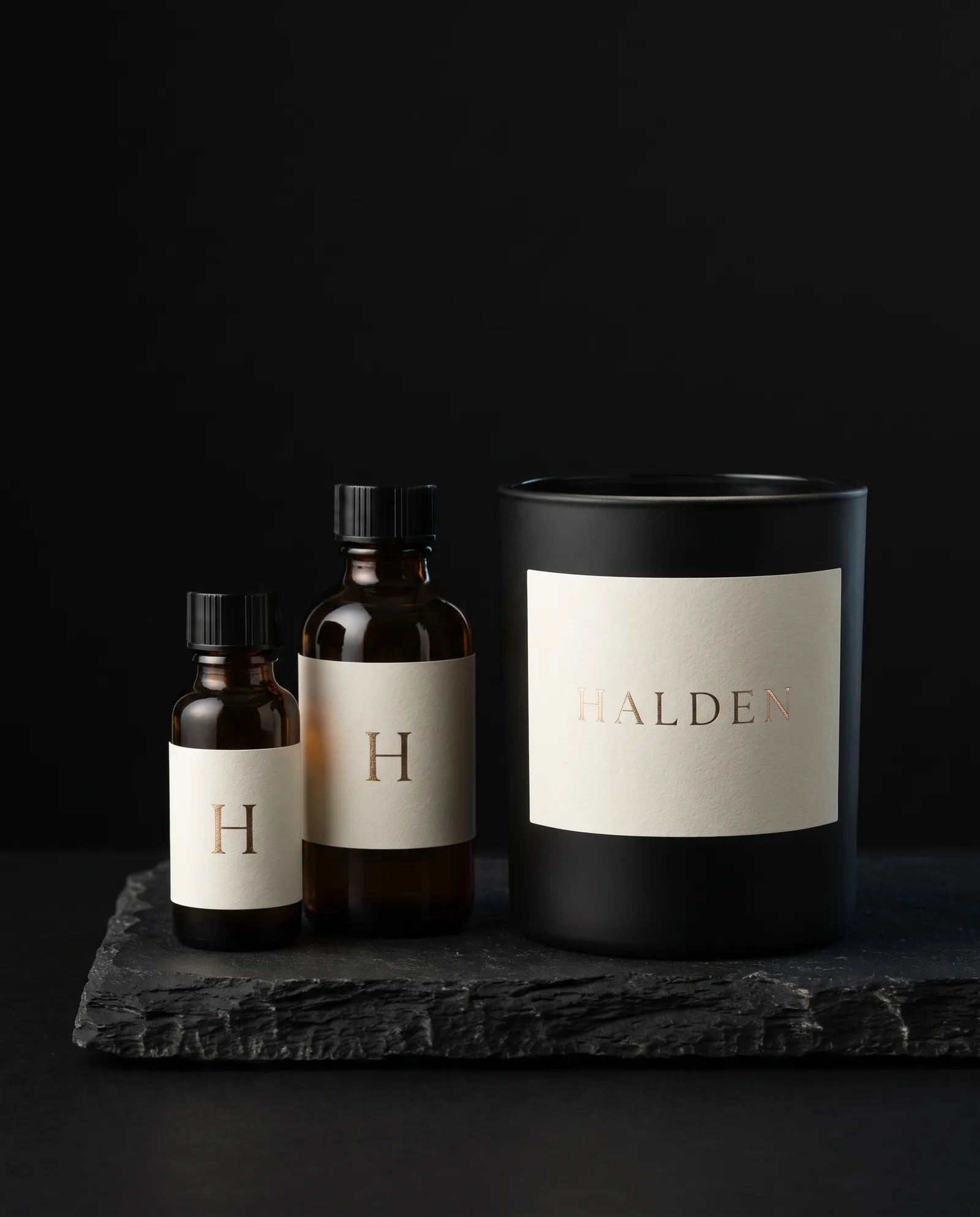 Textured ivory labels with gold foil on two amber bottles and a black candle vessel