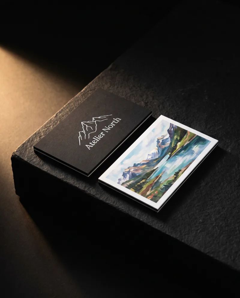 Black duplex business card with silver foil mountain beside white reverse printed with painted landscape