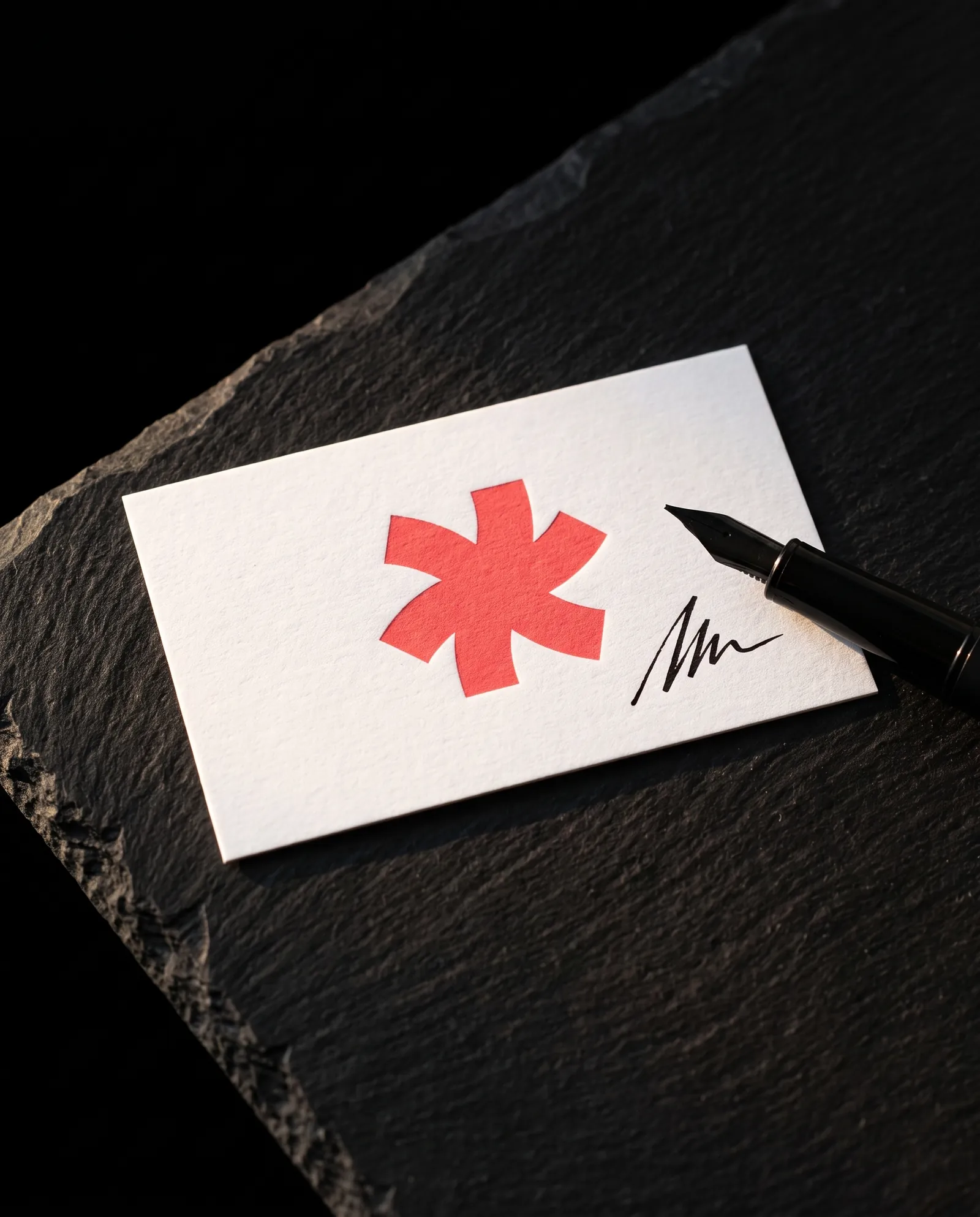 White 14pt uncoated business card with a coral Print Peppermint mark and visible paper tooth, a black fountain pen resting on it