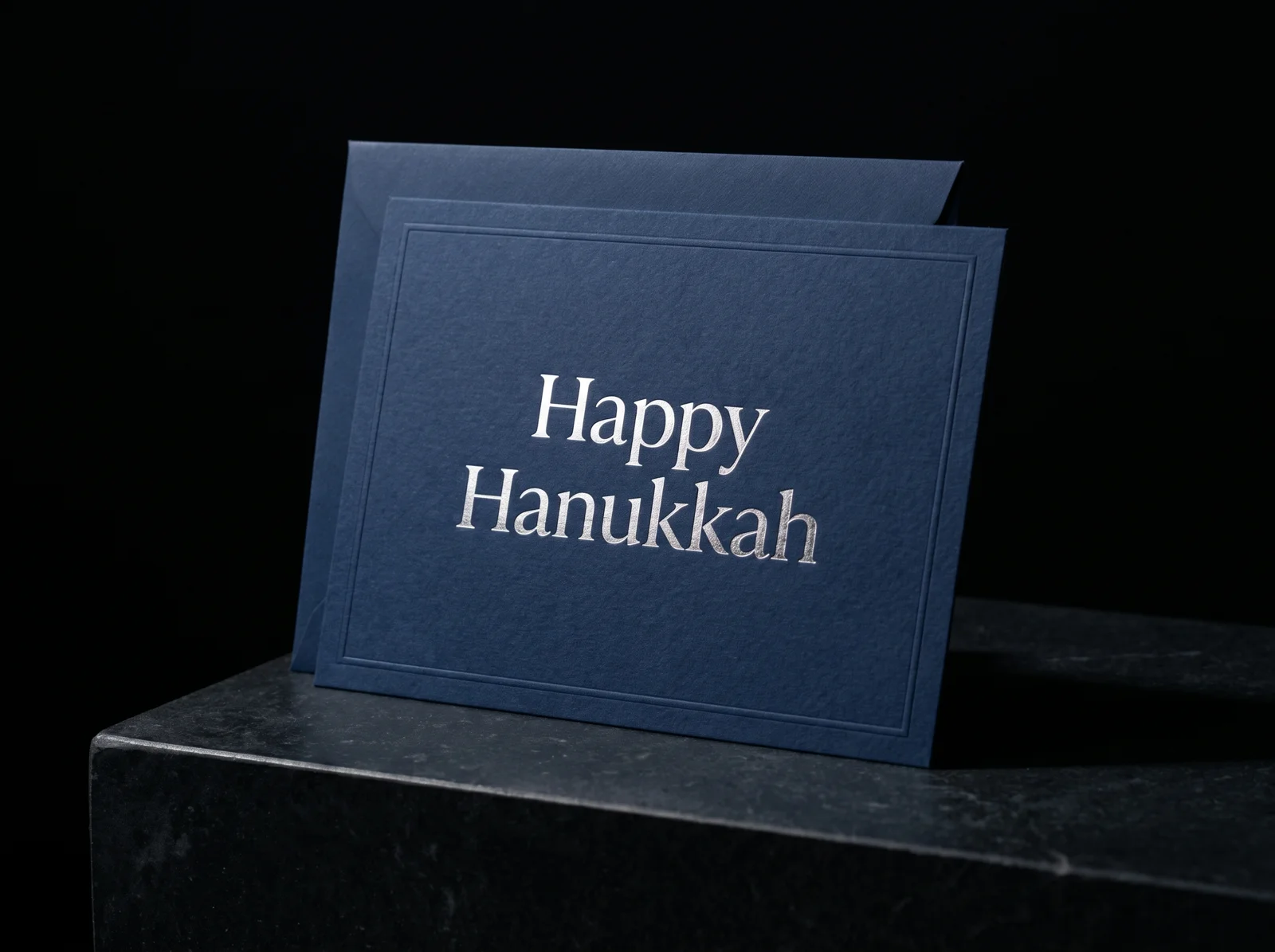Custom Hanukkah card on navy cotton paper with "Happy Hanukkah" in silver foil and a debossed border, with a matching navy envelope
