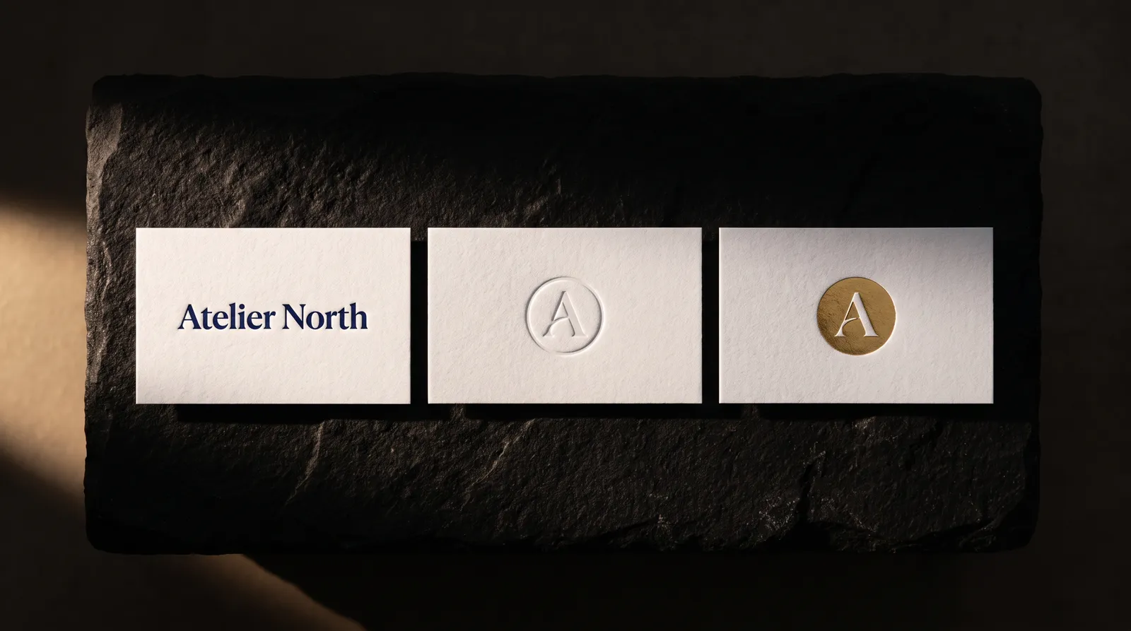 Three cotton business cards side by side: navy letterpress, a blind debossed monogram, and gold hot foil