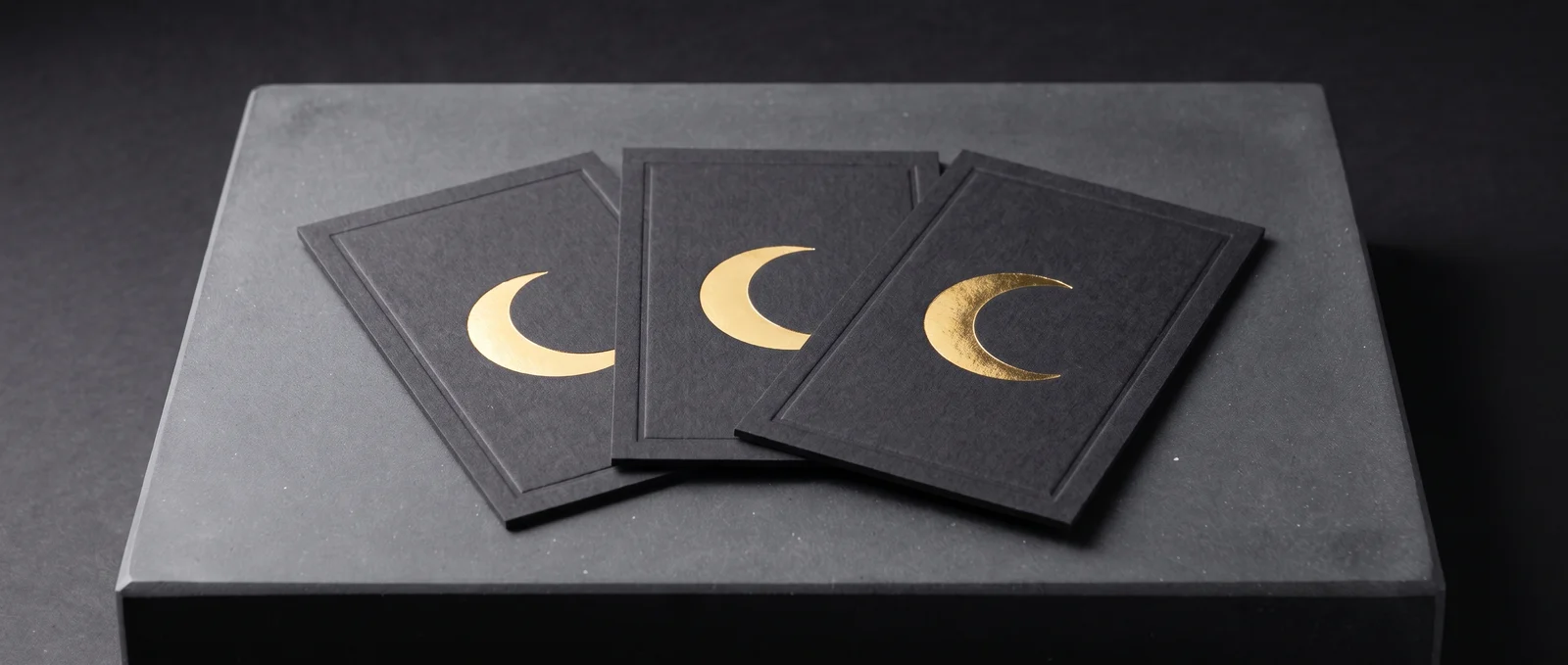 Gold foil on black cotton cards, framed by a blind-debossed border.