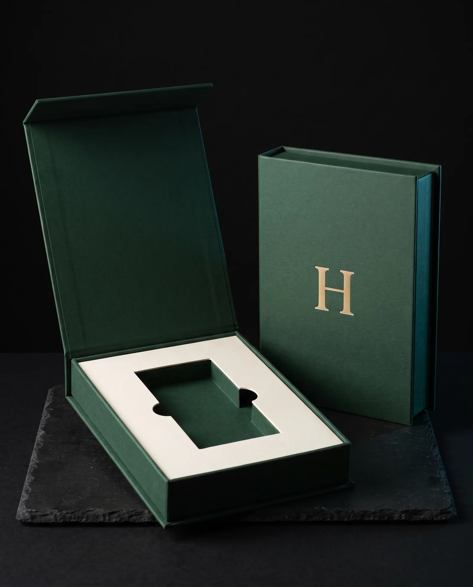 Book-style magnetic box open with an ivory die-cut insert, beside a closed one with a foil monogram
