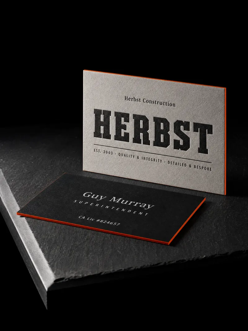 Construction company business card in grey and black duplex with a black letterpress wordmark and a safety-orange edge