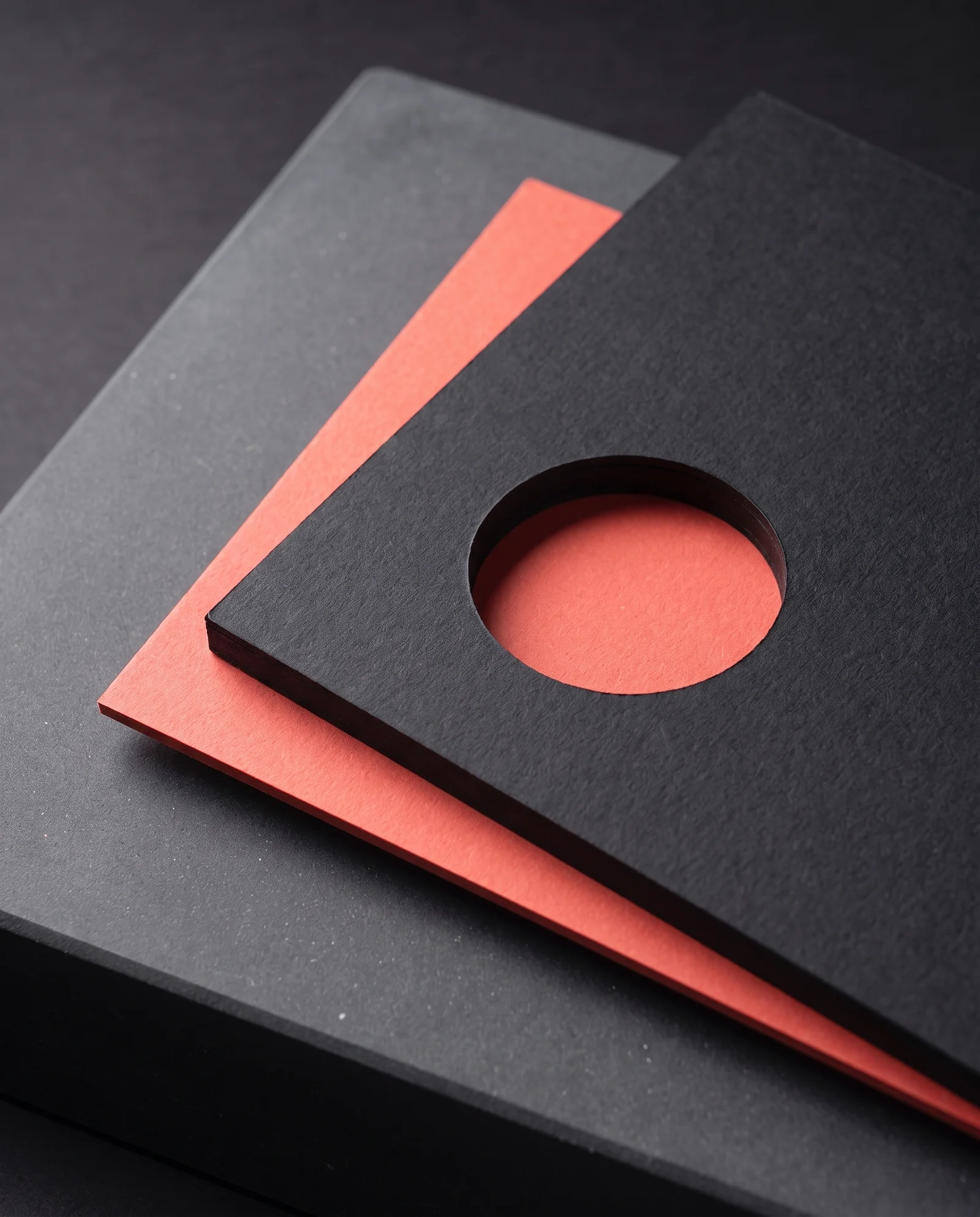 A circular window die-cut through black card, a coral card showing beneath.