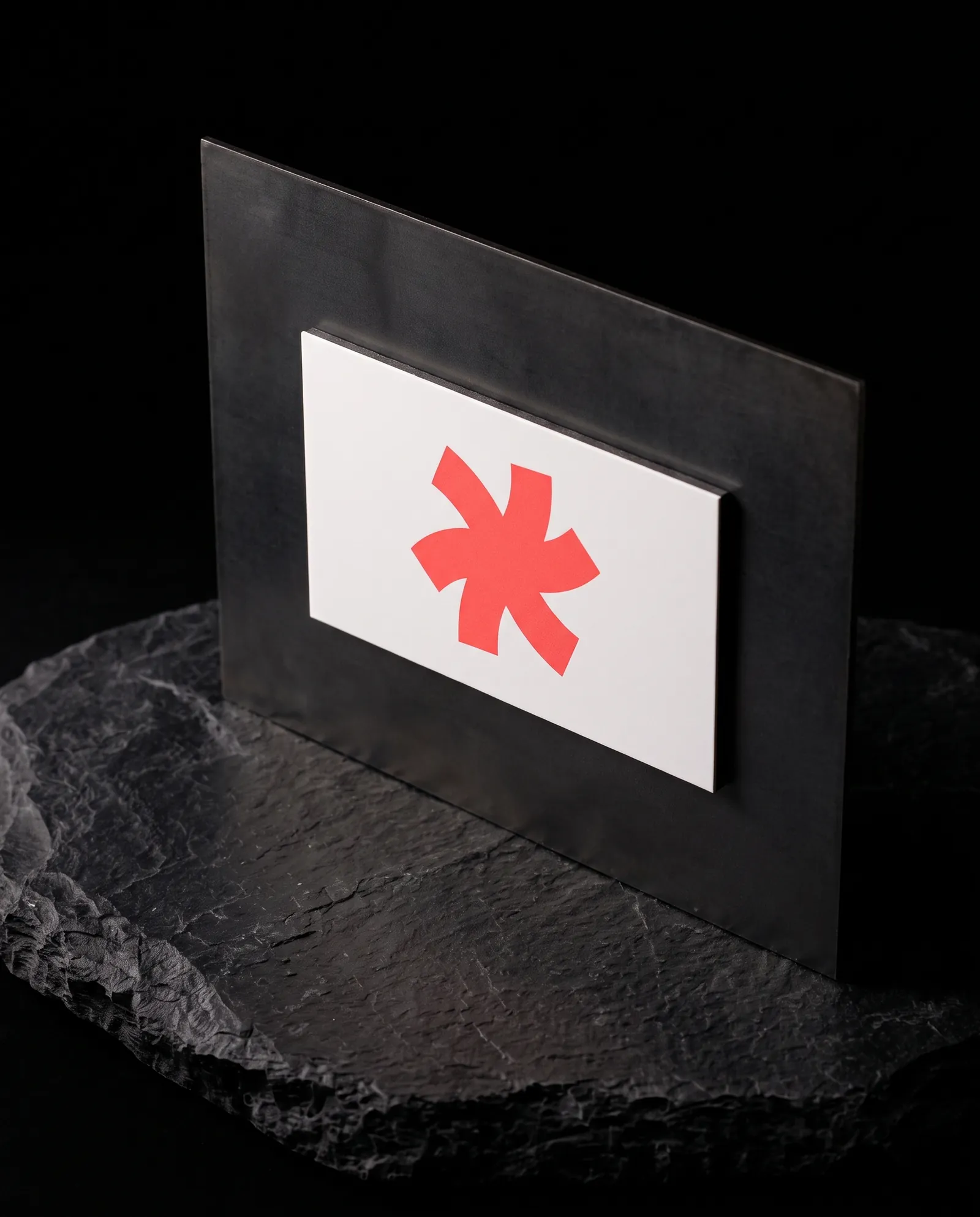 White magnetic business card with a coral Print Peppermint mark held on a blackened steel panel standing on slate