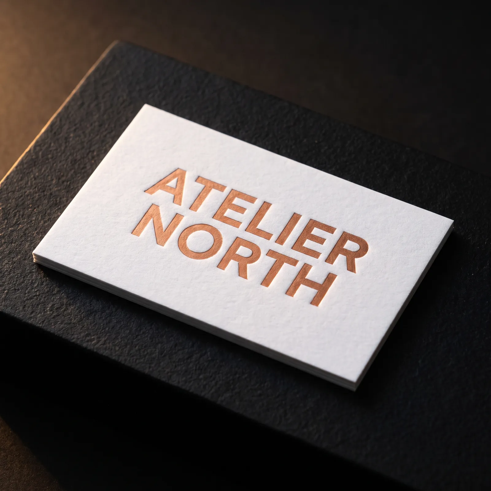 32pt white cotton business card with a copper hot foil Atelier North wordmark on stone