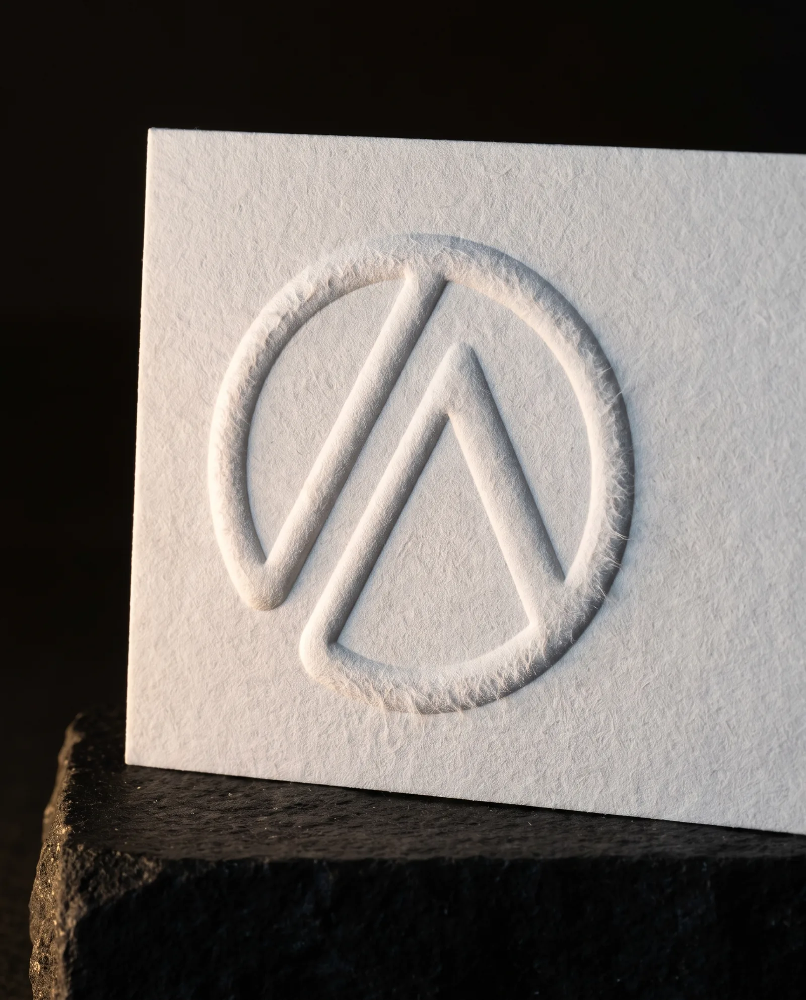 Macro of a blind embossed mark rising from white cotton paper in raking light