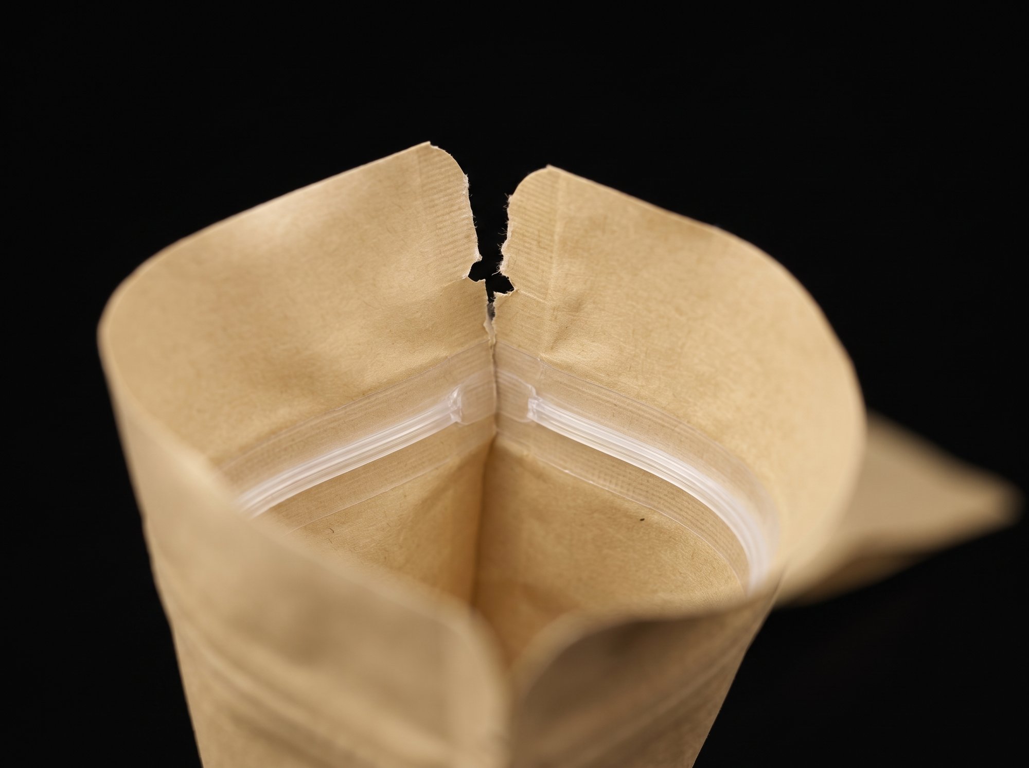 The torn-open top of a kraft pouch showing the tear notch and the press-to-close zipper tracks.