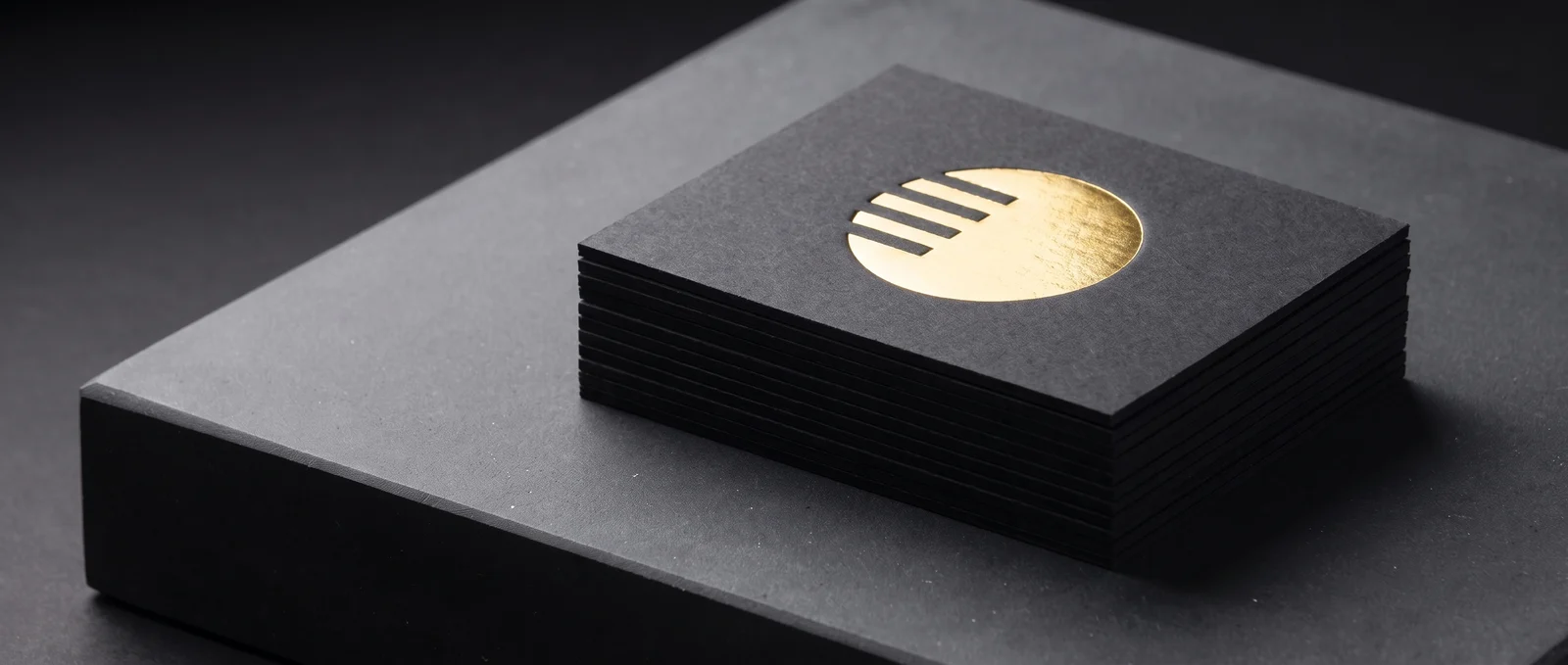 A stack of black cotton cards, the top one hot-foil stamped in mirror gold, pressed into the sheet.