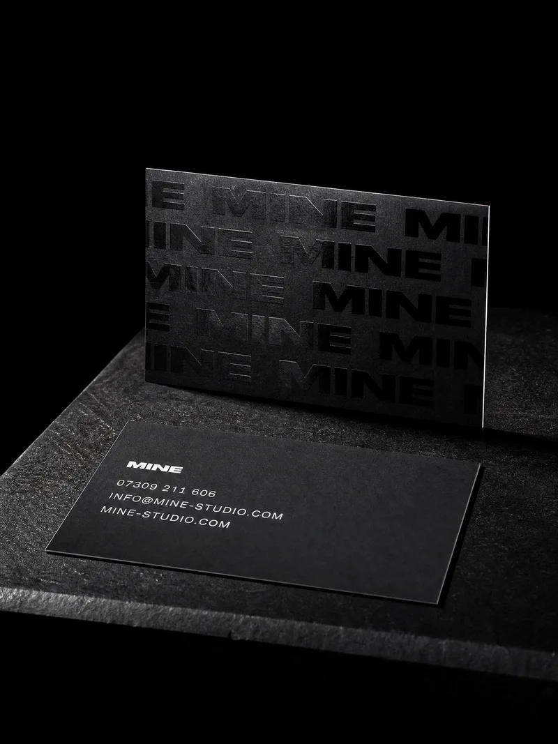 Matte black business card with a repeating wordmark in glossy spot UV catching one streak of light