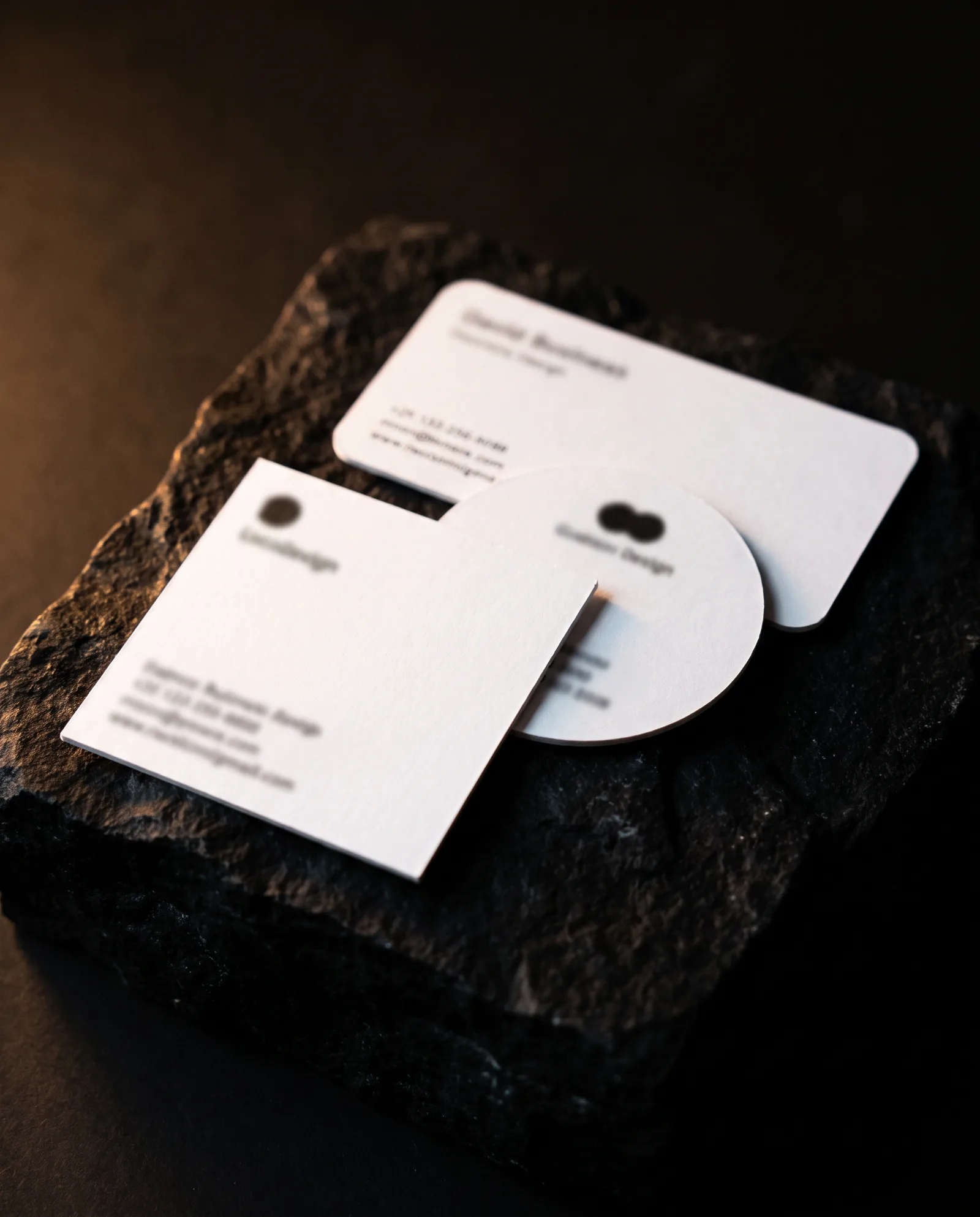 White square, circle and rounded-corner business cards with soft black print on stone