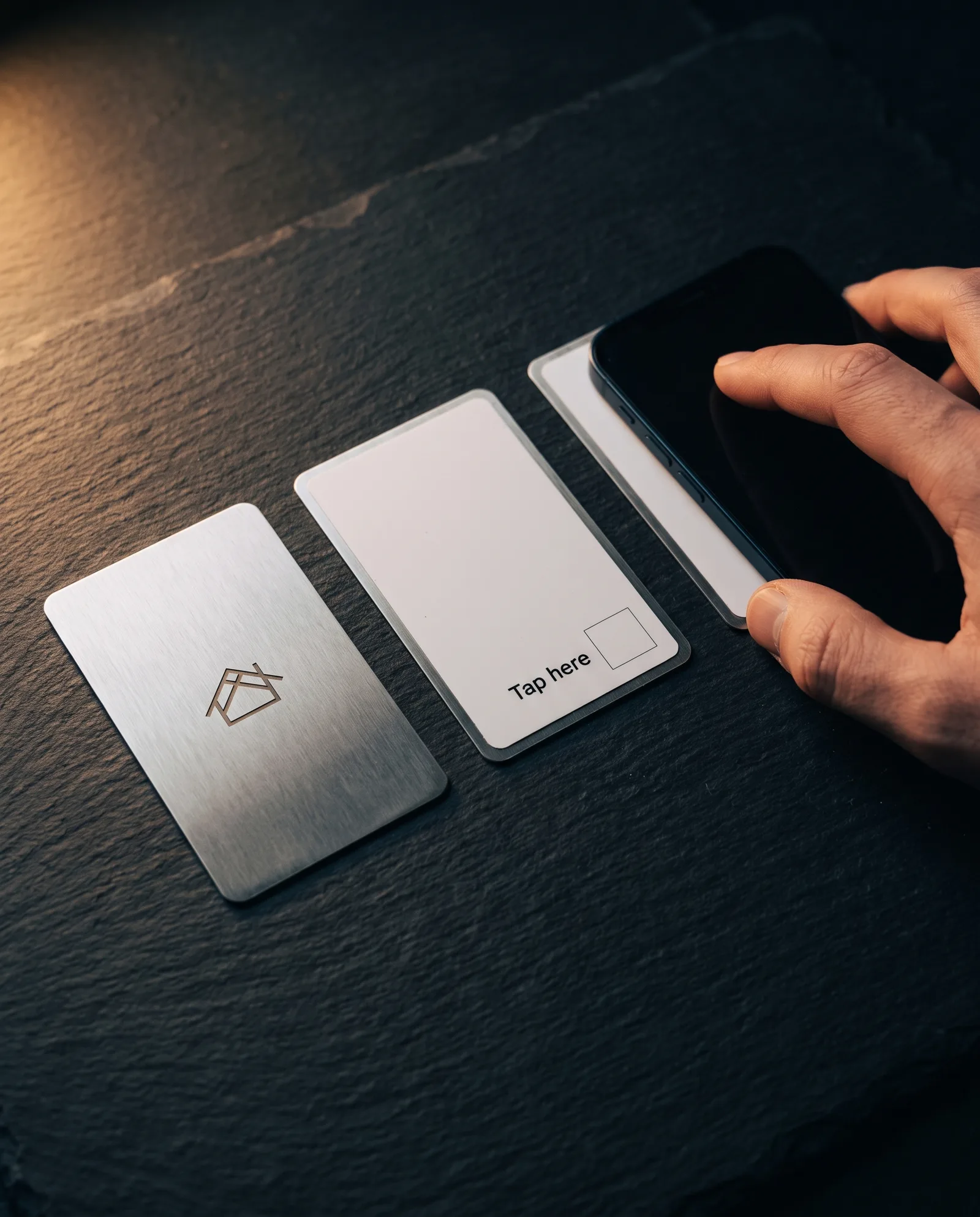 Brushed steel NFC review card beside its printed back marked 'Tap here', with a phone tapping the printed side of a third card