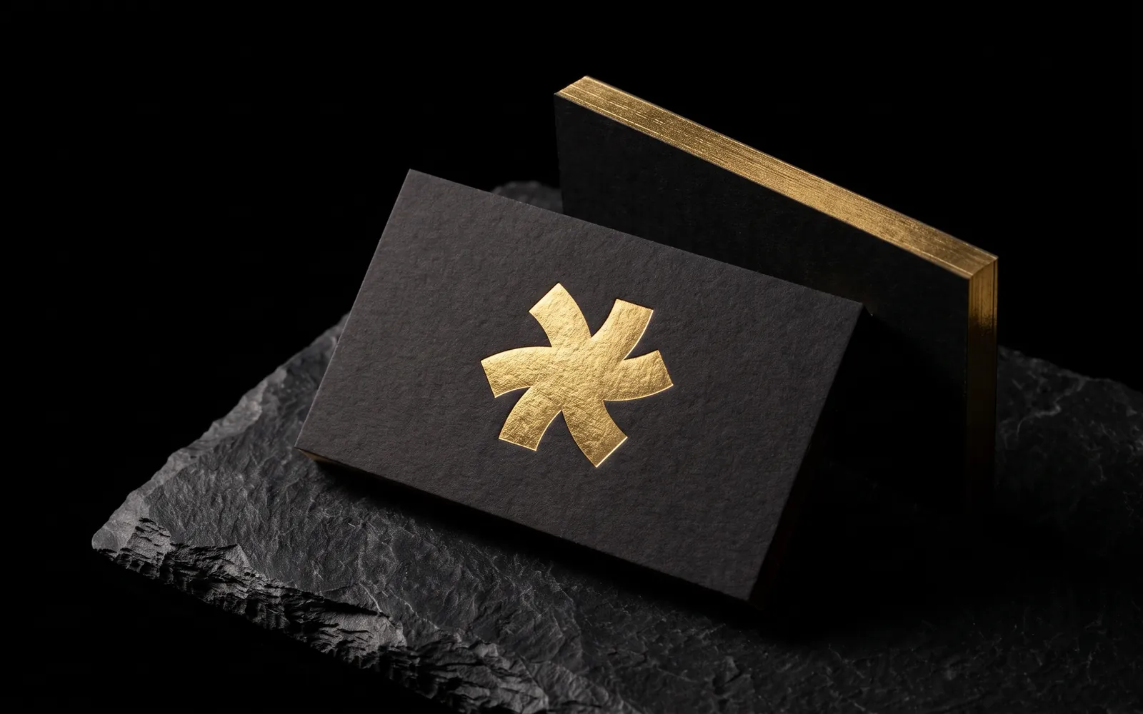Black business cards on dyed-through black cotton: the Print Peppermint mark hot foil stamped in gold, and a second card on edge showing a gold foil edge, on black slate